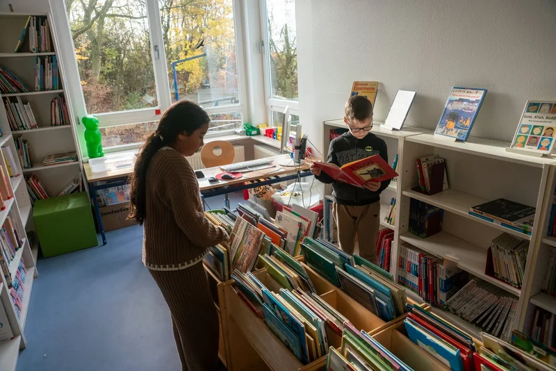 Zwei Kinder suchen Bücher in der Schulbücherei aus.