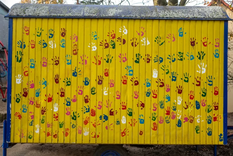 Bunte Handabdrücke auf einem gelben Bauwagen auf dem Schulhof.