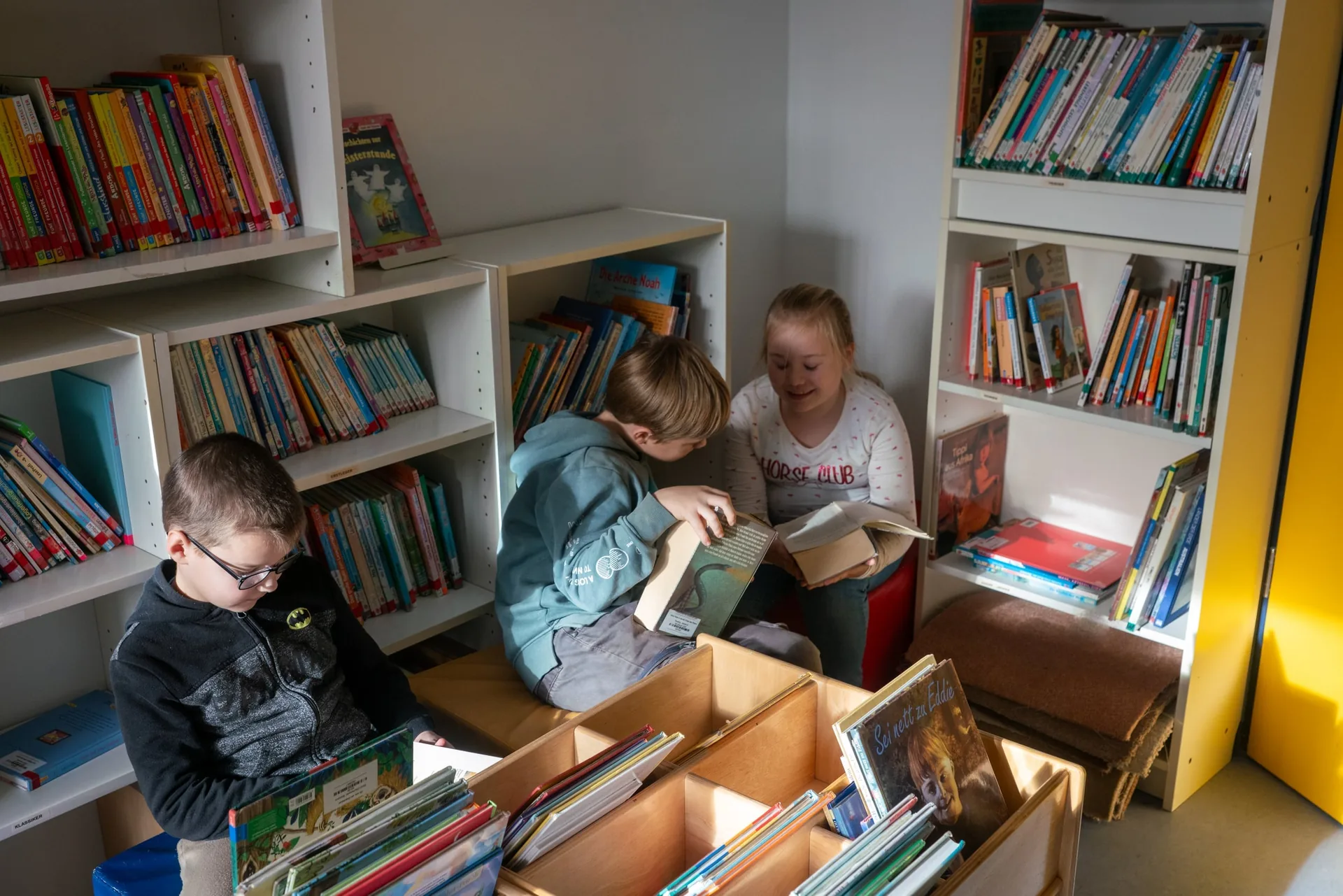 Kinder lesen gemeinsam in einer Sitzecke der Schulbücherei.